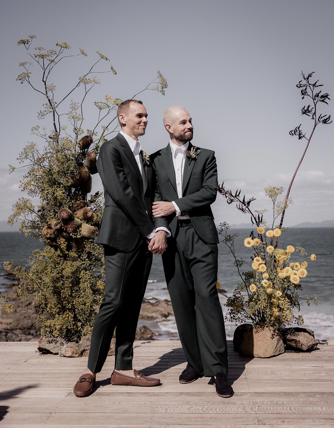 a couple stand in front of a structural display of florals in the middle of their wedding ceremony
